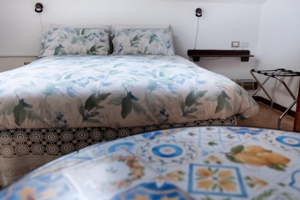 Camera Orchidea mansardata del B&amp;B C'era una volta con letto in primo piano, tavolino con due sedie bianche, angolo caffè con carta da parati botanica e porta aperta sul bagno privato con doccia.