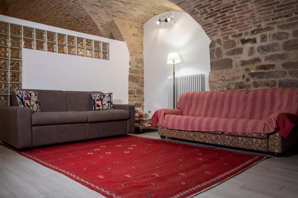 Spacious living room of Domus Romana holiday home featuring traditional stone walls, brick vaulted ceilings, a wooden dining table with chairs, and a cozy lounge area.