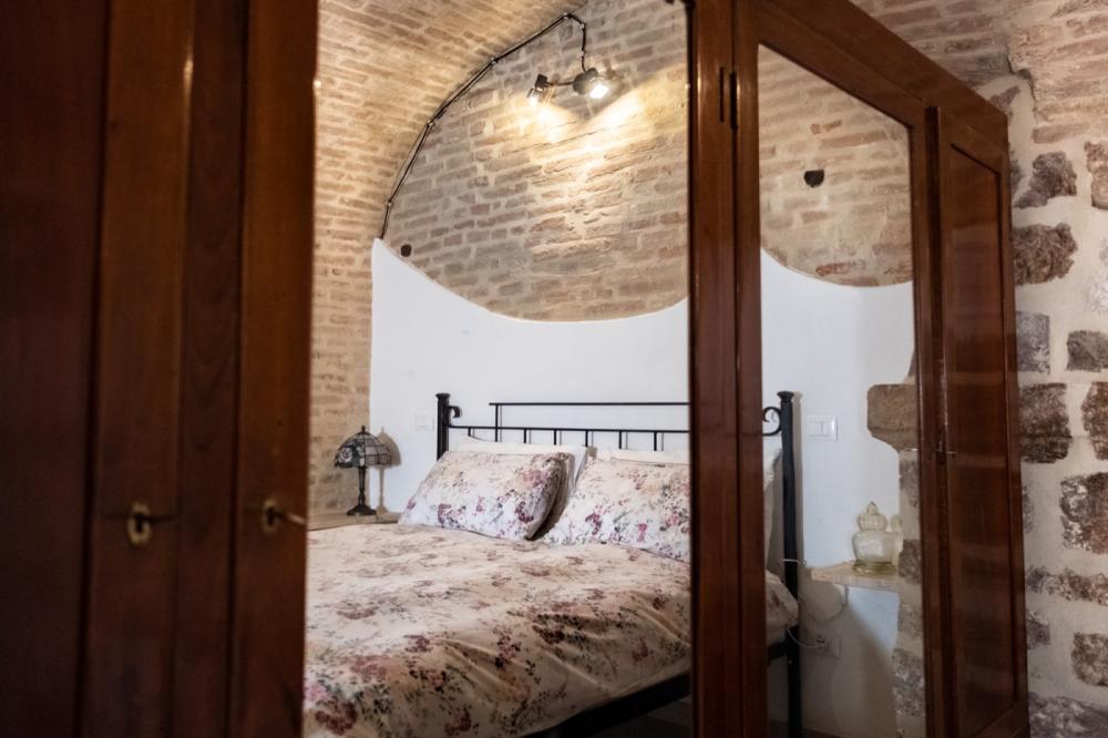 Affascinante camera da letto della casa vacanze Domus Romana con soffitti a volta in mattoncini, letto matrimoniale in ferro battuto e grande armadio antico in legno con specchi.