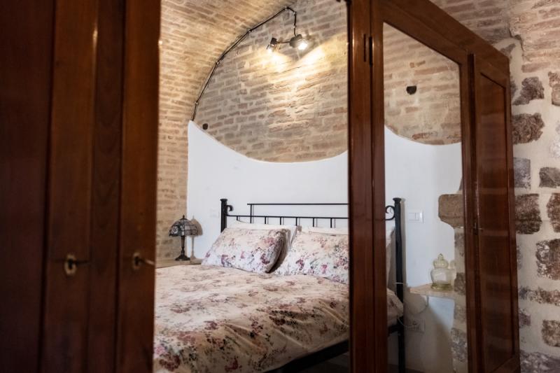 Affascinante camera da letto della casa vacanze Domus Romana con soffitti a volta in mattoncini, letto matrimoniale in ferro battuto e grande armadio antico in legno con specchi.