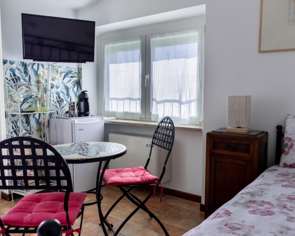 Luminoso angolo relax nella Camera Papavero del B&amp;B C'era una volta, completo di tavolino da caffè in vetro, sedie in metallo con cuscini rossi e TV a parete.