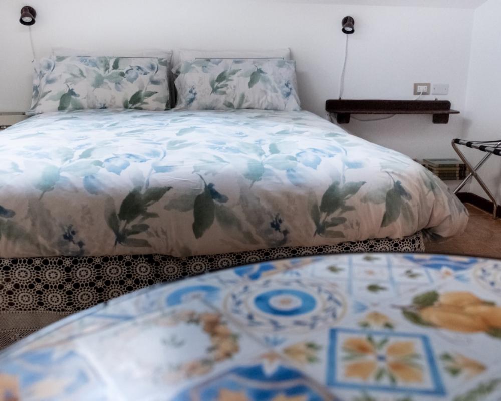 Camera Orchidea mansardata del B&amp;B C'era una volta con letto in primo piano, tavolino con due sedie bianche, angolo caffè con carta da parati botanica e porta aperta sul bagno privato con doccia.
