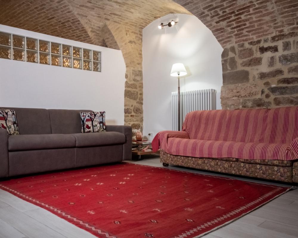 Spacious living room of Domus Romana holiday home featuring traditional stone walls, brick vaulted ceilings, a wooden dining table with chairs, and a cozy lounge area.