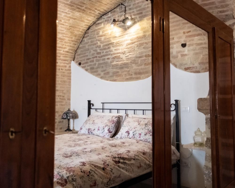 Affascinante camera da letto della casa vacanze Domus Romana con soffitti a volta in mattoncini, letto matrimoniale in ferro battuto e grande armadio antico in legno con specchi.