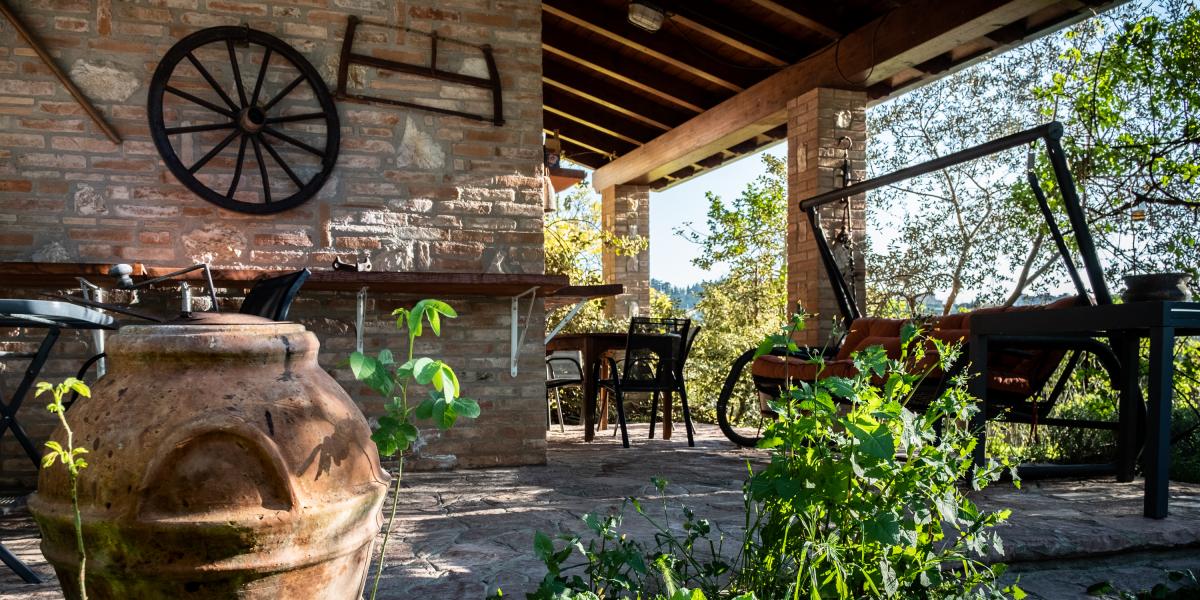 Cozy outdoor porch and giardino relax area at C'era una volta B&amp;B, featuring a small table with chairs next to a brick wall decorated with an old cartwheel and rustic tools.