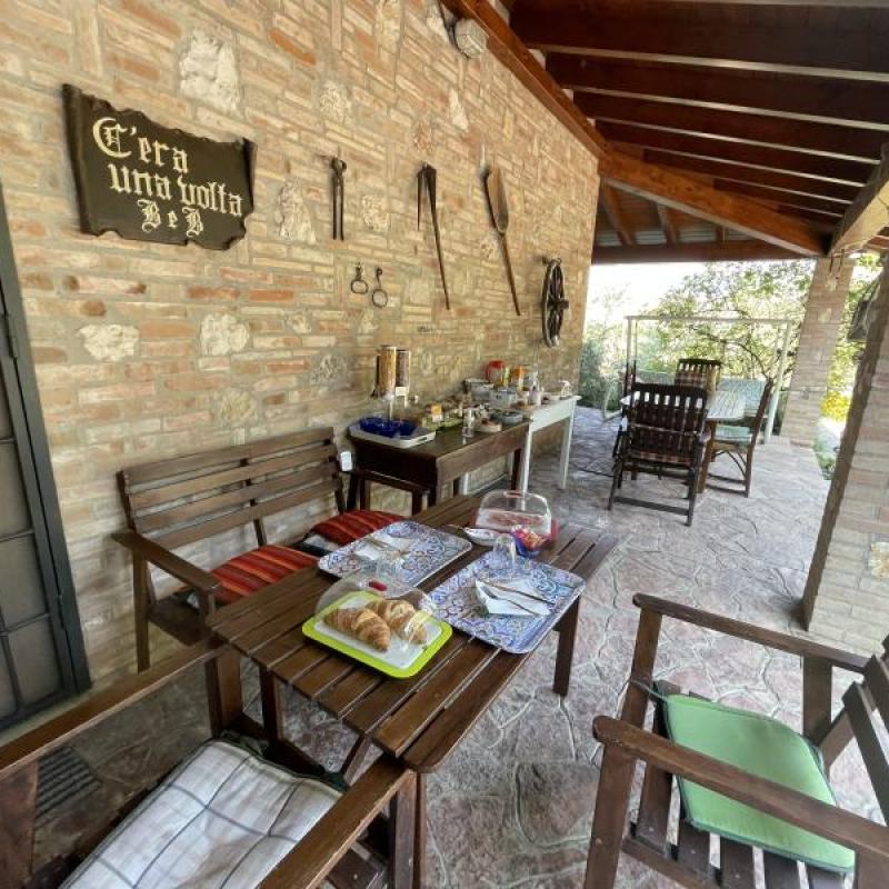 Un incantevole portico con angolo relax in giardino, decorato con antichi strumenti della tradizione contadina.